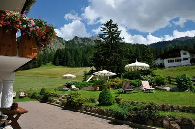 a garden with chairs and umbrellas and a house at Garni Hotel Iris in Selva di Val Gardena