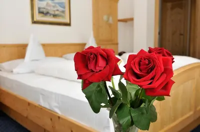 two red roses in a vase on a bed at Garni Hotel Iris in Selva di Val Gardena