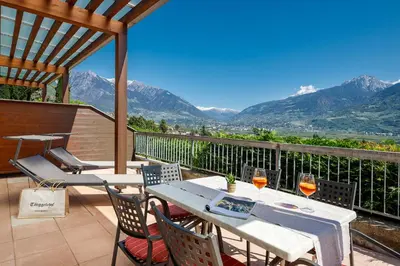 a table with wine glasses on a balcony with mountains at Hotel Törggelehof in Cermes