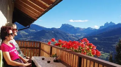 a man and woman sitting on a balcony with a view of mountains at Rasiglerhof in Villandro