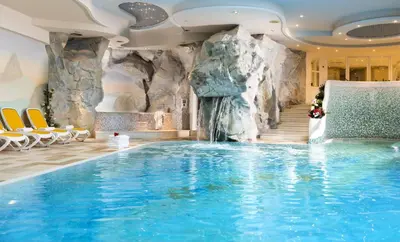 a swimming pool in a hotel with a waterfall at Alpen Hotel Corona in Vigo di Fassa