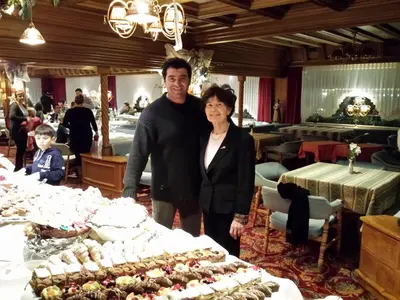 a man and woman standing next to a table with food at Alpen Hotel Corona in Vigo di Fassa