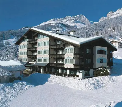 a large building in the snow with mountains in the background at Alpen Hotel Corona in Vigo di Fassa
