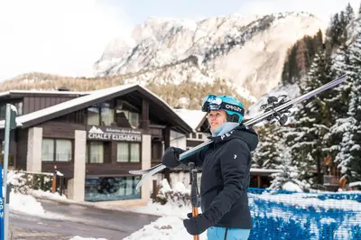 a man holding skis in front of a lodge at Chalet Elisabeth dolomites alpin & charme in Selva di Val Gardena