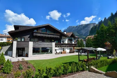 a house with a large yard with a green lawn at Chalet Elisabeth dolomites alpin & charme in Selva di Val Gardena