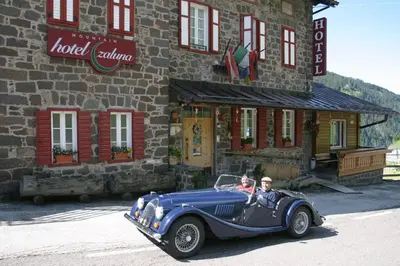 two people in a blue car in front of a building at Small & Lovely Hotel Zaluna in Predazzo