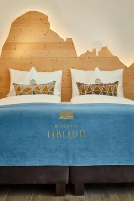 a bed with a blue blanket on top of it at Hotel Tabladel in Colfosco