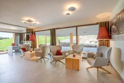 a living room with chairs and tables and windows at Hotel Seelaus in Alpe di Siusi