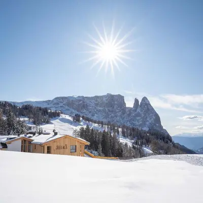 a house on a snowy mountain with the sun in the sky at Hotel Seelaus in Alpe di Siusi