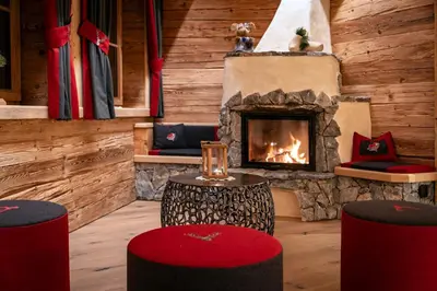 a living room with a fireplace and two stools at Chalets Almdorf Haidenberg in Brunico