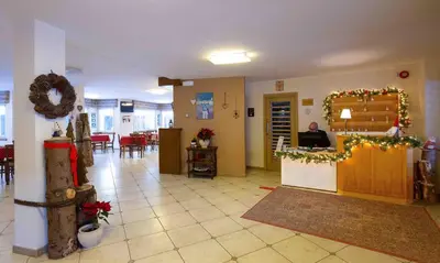 a lobby with christmas decorations and a man sitting at a counter at Santa Maria ad Nives in Canazei