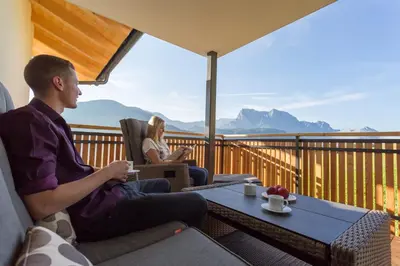 a man and woman sitting on a balcony with a view of mountains at Tschörlerhof in Barbiano