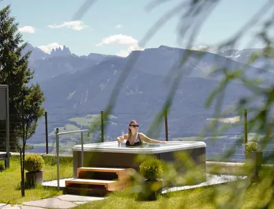 a woman in a bath tub with mountains in the background at Granpanorama Wellnesshotel Sambergerhof Superior in Villandro
