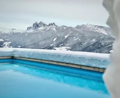 a blue pool with mountains in the background at Granpanorama Wellnesshotel Sambergerhof Superior in Villandro