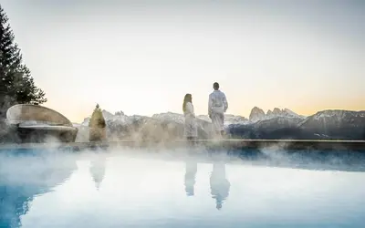 a man and a woman standing in front of a pool of water at Granpanorama Wellnesshotel Sambergerhof Superior in Villandro