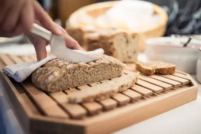 a person cutting bread with a knife on a cutting board at Hotel Alpenhof in Ultimo