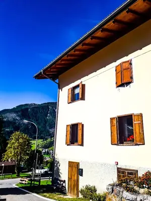 a white house with wooden windows and mountains in the background at Appartamento Vista Dolomiti by GoNewLocation in Moena