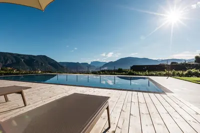 a swimming pool with a wooden deck and the sun at Egarter in Appiano sulla Strada del Vino