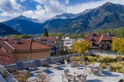 a patio with tables and chairs and mountains in the background at Residence Villa Hedy in Merano