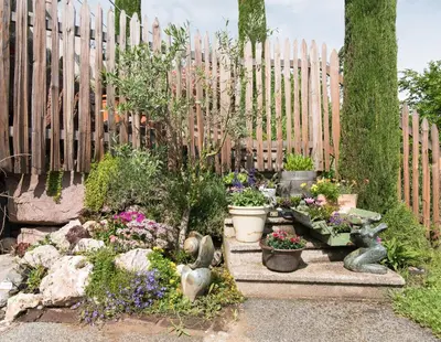 a garden with flowers and statues in front of a fence at Kreuzstein Bed&Breakfast in Appiano sulla Strada del Vino