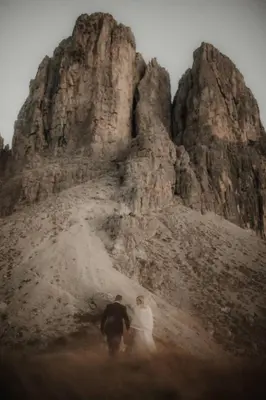 a bride and groom walking in front of a mountain at Chalet Roenn in Colfosco