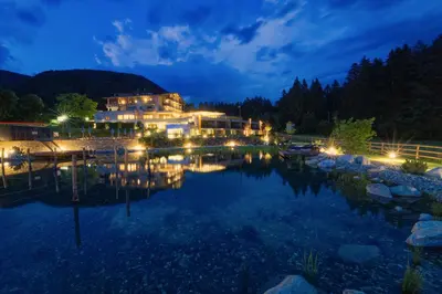 a large house with lights on the water at night at Bonfanti Design Hotel in Chienes
