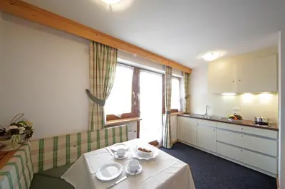 a room with a table and a kitchen with a window at Garnì Lasteis B&B - apartments in La Villa