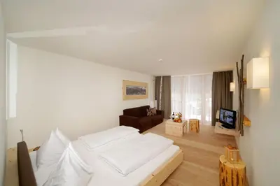 a bedroom with a white bed and a living room at Vitalhotel Rainer in Ultimo