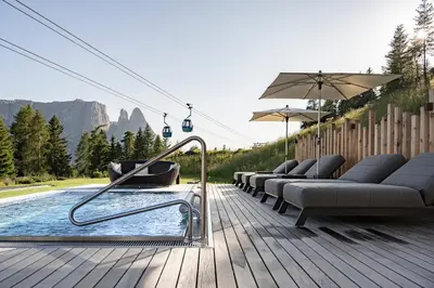 a pool with chairs and an umbrella on a wooden deck at Hotel Schmung in Alpe di Siusi