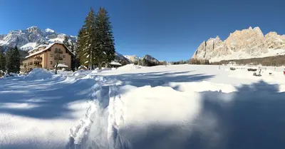 a snow covered field with a house and mountains at Boutique Hotel Villa Blu Cortina D'Ampezzo in Cortina dʼAmpezzo