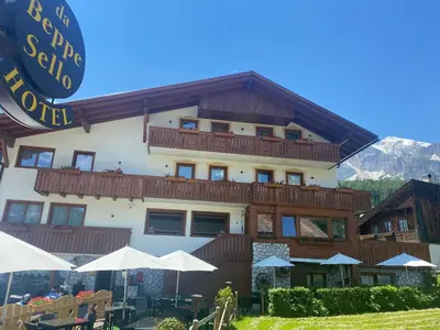 a large building with tables and umbrellas in front of it at Hotel da Beppe Sello in Cortina dʼAmpezzo