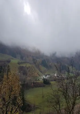 a misty valley with houses and trees on a hill at Temblhof in Vipiteno