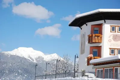 a building with a snow covered mountain in the background at La Montanina Hotel in Val di Non in Malosco