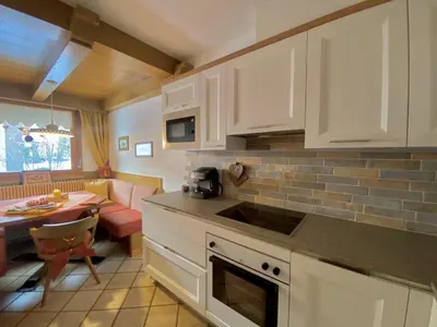 a kitchen with white cabinets and a living room at Residence Lastè in Moena