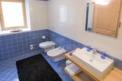 a blue tiled bathroom with a toilet and a sink at Villa Edelweiss in Alleghe