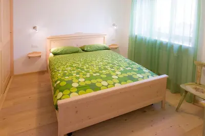 a bedroom with a wooden bed with a green comforter at Villa Edelweiss in Alleghe