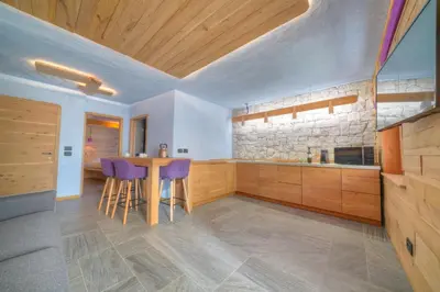 a kitchen with wooden cabinets and a table with purple stools at Tana del Picchio in Falcade