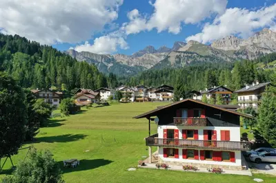 a house in a field with mountains in the background at Tana del Picchio in Falcade