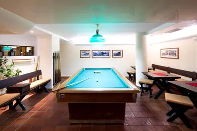 a pool table in a room with tables and benches at Hotel Portavescovo in Arabba