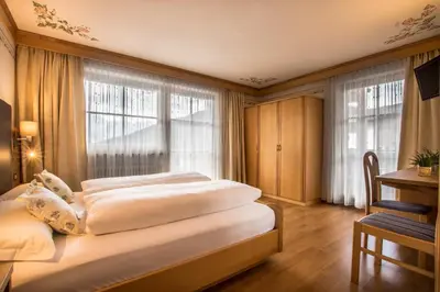a bedroom with two beds and a desk and windows at Ciasa Montanara in La Villa