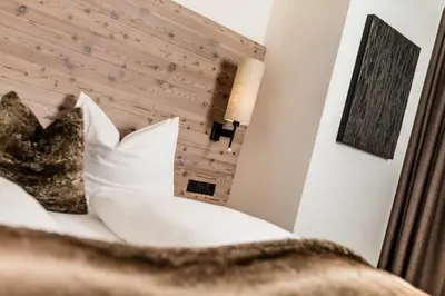 a bed with white pillows and a wooden headboard at ArtHotel Anterleghes - Gardenahotels in Selva di Val Gardena