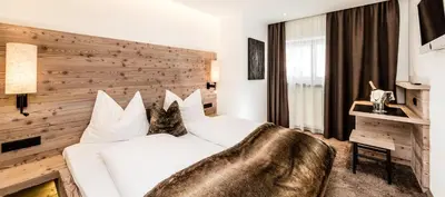 a bedroom with a white bed and a wooden wall at ArtHotel Anterleghes - Gardenahotels in Selva di Val Gardena