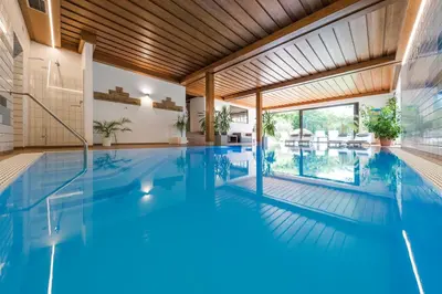 an indoor swimming pool with blue water in a house at Hotel Weger in Tirolo