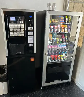 a soda vending machine next to a drink cooler at Ploner villaggio Turistico in Dobbiaco