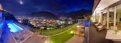 a balcony with a view of a city at night at La Pergola PanoramaSuites in Tirolo