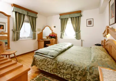 a bedroom with a bed and a desk and two windows at Hotel Regina in Cortina dʼAmpezzo