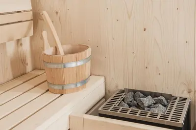 a sauna with a wooden bucket and some rocks at Aquila Dolomites Residence in Ortisei
