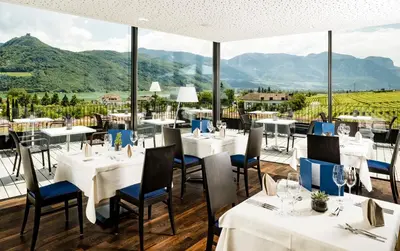 a restaurant with tables and chairs with mountains in the background at Hotel Thalhof am See in Caldaro