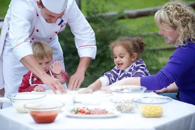 a woman and two children standing around a table with food at Familienhotel Maria in Obereggen