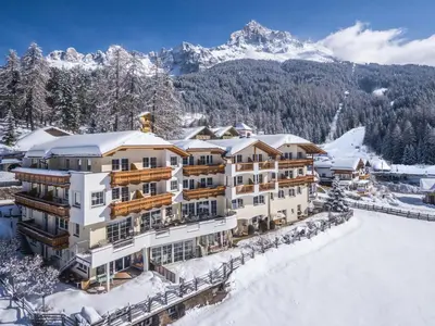 a hotel in the snow with mountains in the background at Familienhotel Maria in Obereggen